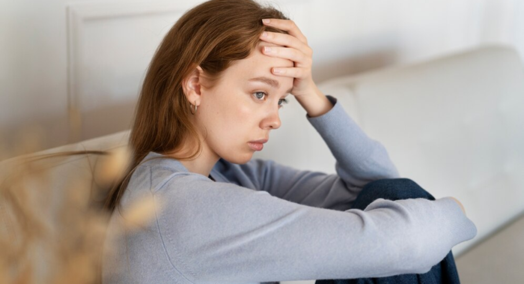 A young woman sitting on a couch looking distressed and emotionally exhausted with her hand on her forehead, illustrating the symptoms that require expert depression treatment in Mohali by Dr. Parag Sharma.