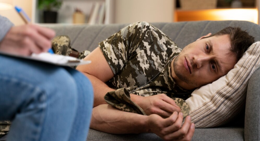 A distressed man lying on a therapy couch while a psychiatrist takes notes, representing the clinical environment for expert childhood trauma and PTSD care in Mohali."
