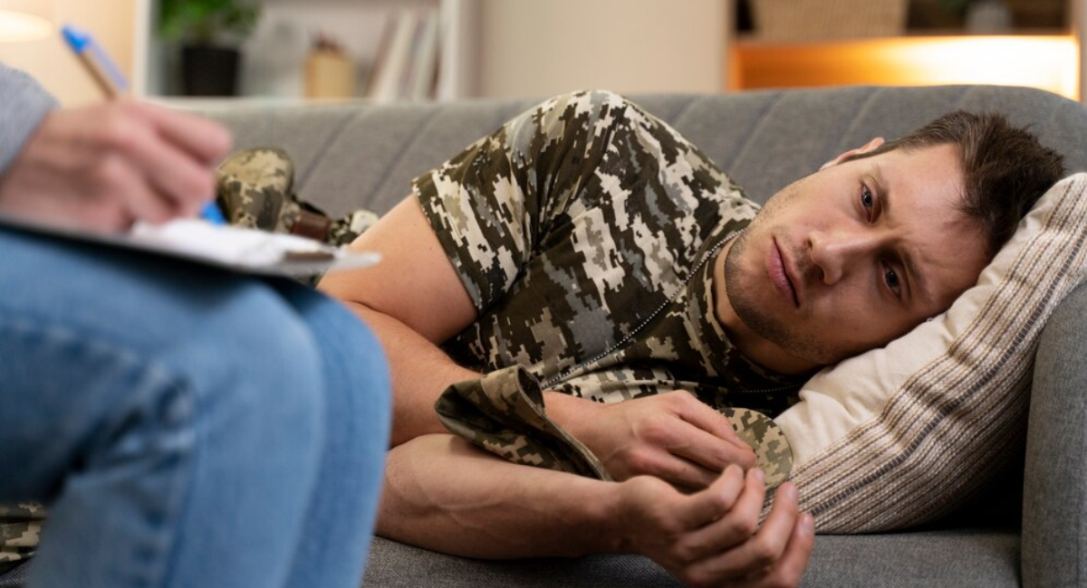 A distressed man lying on a therapy couch while a psychiatrist takes notes, representing the clinical environment for expert childhood trauma and PTSD care in Mohali."